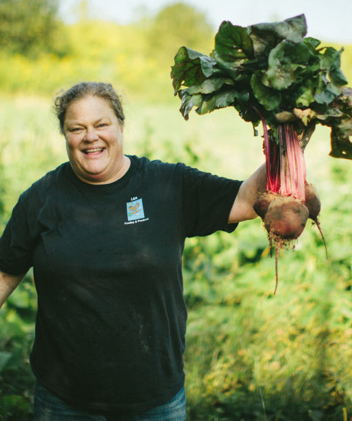 Smiling woman wearing a black t-shirt holds up a rutabaga proudly